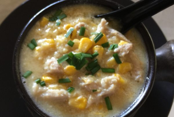 Chicken and corn soup served in a black bowl garnished with sliced green shallots by cookingmealsforone.com