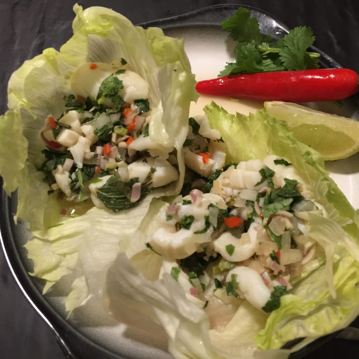 Quick Thai Squid Salad by cookingmealsforone.com Is made of scored squid hoods cooked in lime juice-fish sauce-red chilli and water for 2 minutes then cooled and combined with chopped mint-coriander-lemongrass-then spooned into a crisp lettuce cup