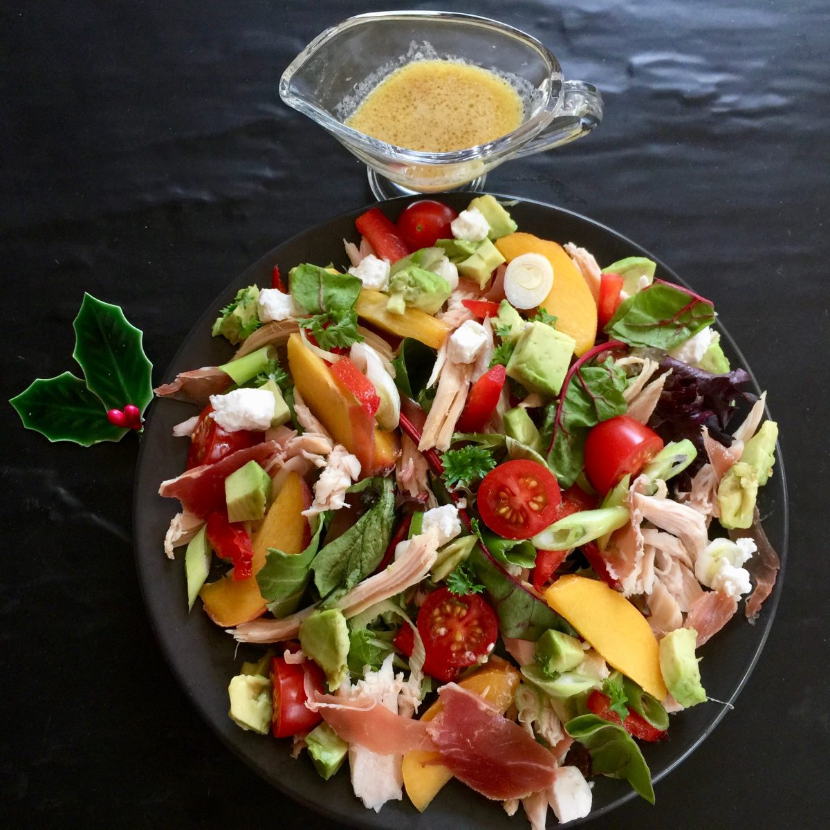 a vibrant salad filled with avocado, lettuce, cooked chicken, wedges of fresh peaches, halved cherry tomatoes, red chilli, mixed lettuce, baby spinach, rocket, avocado, prosciutto, goats cheese, green shallots, served with a dijon mustard vinegarette