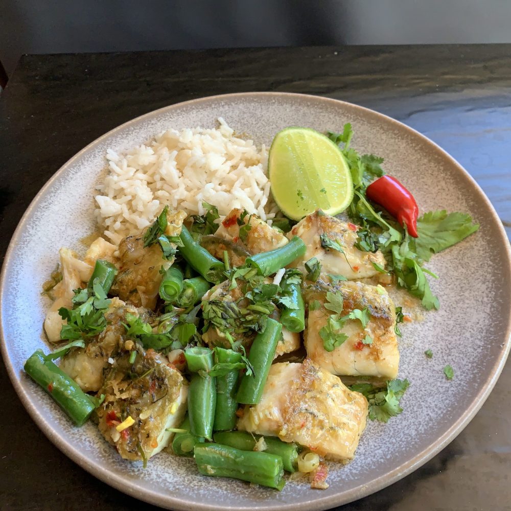 A very tasty plate full of curry flavoured fish bites, stir fried with green bean buttons , served with cooked rice and sprinkled with freshly chopped coriander and garnished with sprig of coriander and red chilli with a wedge of lime.