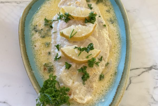 Creamy Lemon Baked Fish For One: A white fillet of fish cooked in a buttery, garlic, mustard flavoured coconut creamy sauce,topeed with freshly chopped parsley. Served on a blue plate with a wedge of lemon. by cookingmealsforone.com