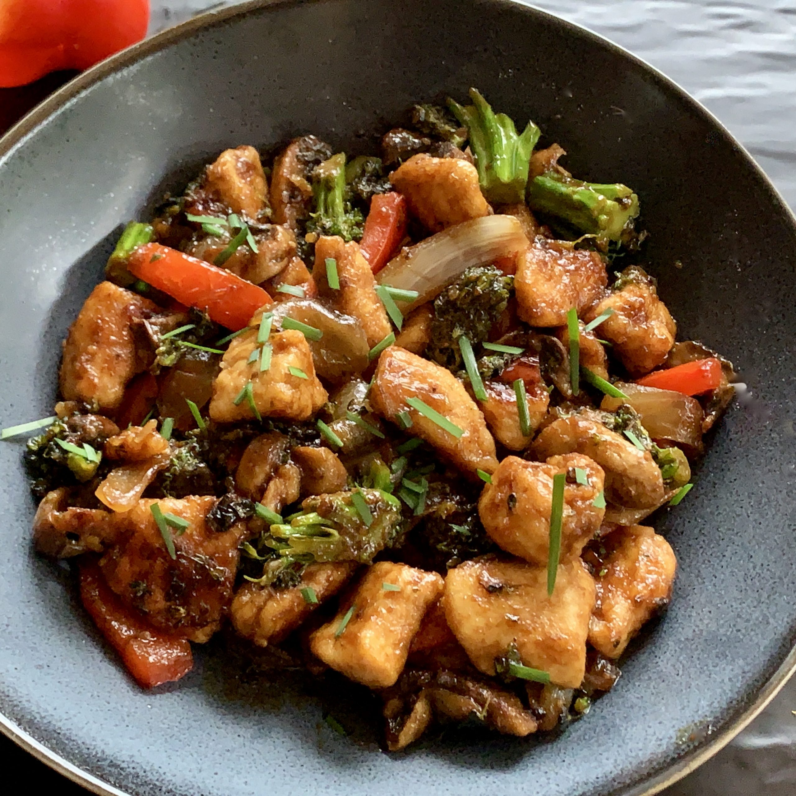 Chicken and Broccolini Stir Fry for One. A bowl of healthy chicken chunks red capsicum, brocollini and chivess, coated in a tasty sauce and cooked in 20 minutes