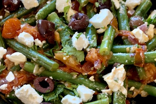 A delicious combination of cooked green beans in a garlic, onion and tomato sauce and garnished with chopped kalamata olives, parsley and crumbled feta served in a black bowl. by cookingmealsforone.com